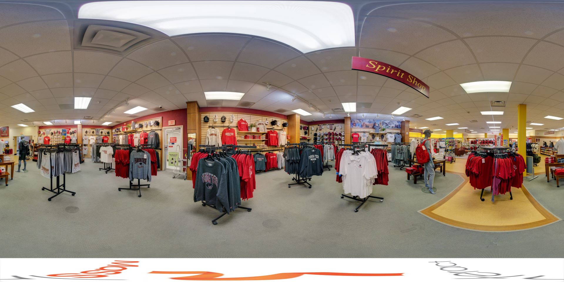 The panoramic image shows a well-organized bookstore featuring Florida Tech apparel in red, gray, and white. Neatly arranged racks and shelves display shirts, hoodies, and other merchandise. The store is brightly lit, with a welcoming atmosphere, and includes a mannequin wearing a red backpack